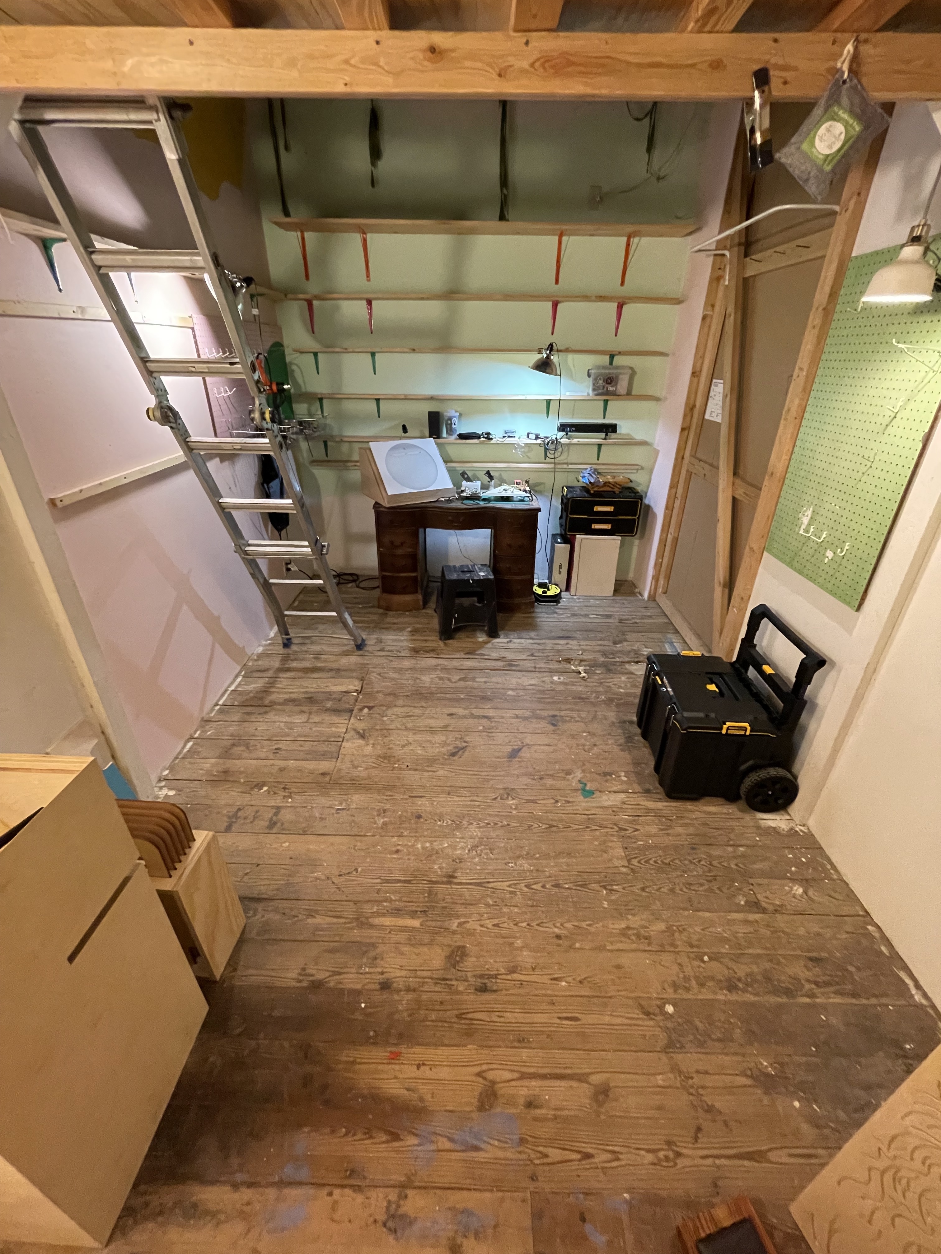 an art studio workspace with rough wooden warehouse floors, a ladder, shelving, a desk